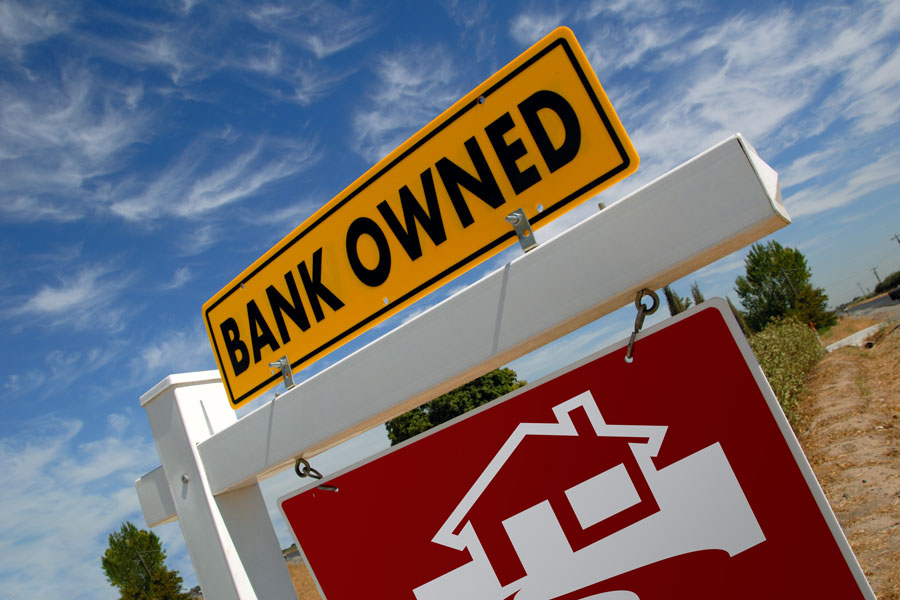 Bank Owned Real Estate Sign and House with American Flag in the Background.