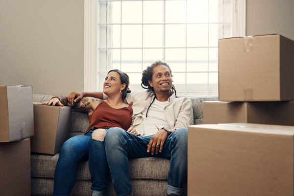 Moving, interracial couple and homeowner on sofa for mortgage, real estate or boxes. Living room, investment and happy woman with man for residence, property rent or relocation in new apartment