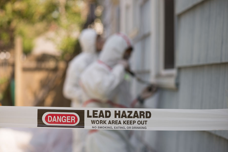 Workers in protective gear perform lead-safe renovation procedures at a residential property