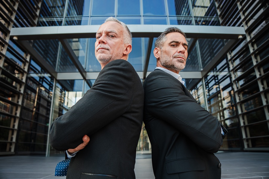 Two confident businessmen standing back to back, displaying determination and strength in a competitive business world, embodying leadership qualities and a partnership in their professional endeavors